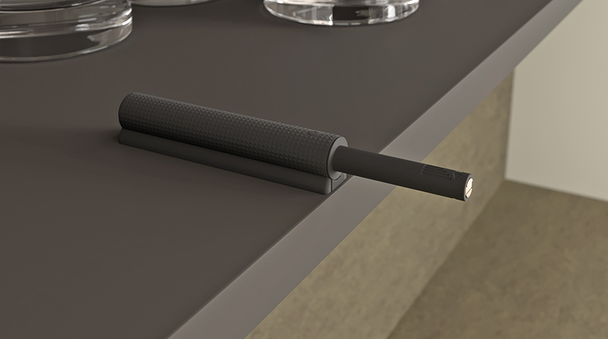 Närbild på ett mörkt K Push Tech Texture adapterhus med utskjutande trycklås vid kanten av en möbelpanel.
